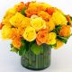 Lush bouquet of two to four dozen vibrant yellow and orange roses, elegantly arranged in a transparent glass vase, reflecting the warm, sunny hues of the flowers