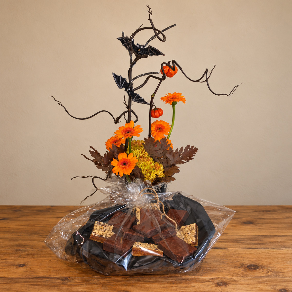Halloween flower arrangement with orange gerberas, mini pumpkins, curly branches, and decorative bats